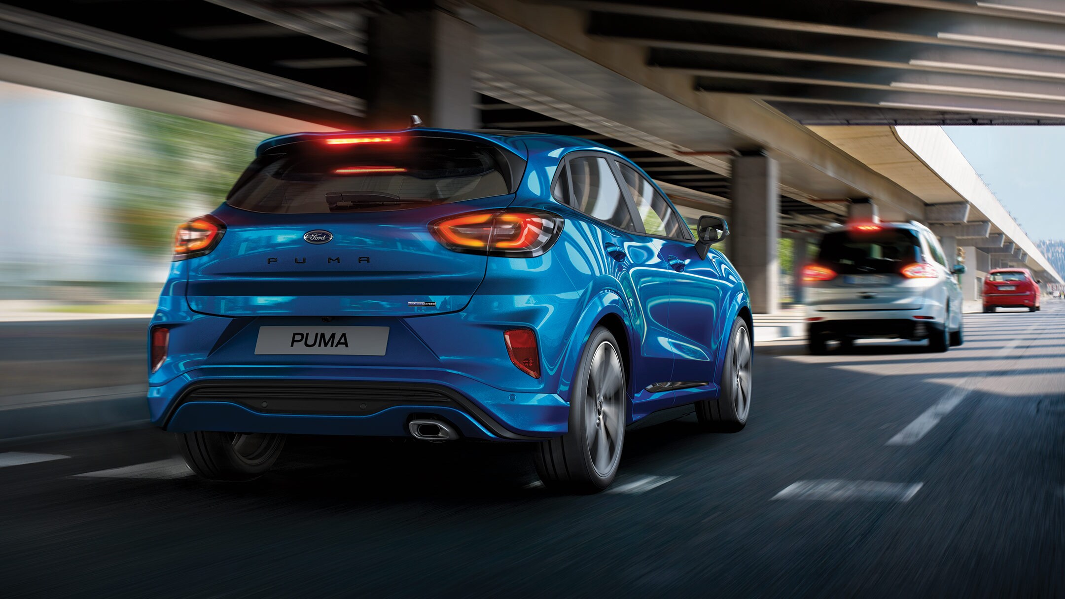 Ford Puma in Blau. Fahrend auf Straße mit aktiven Bremsleuchten hinter grauem PKW