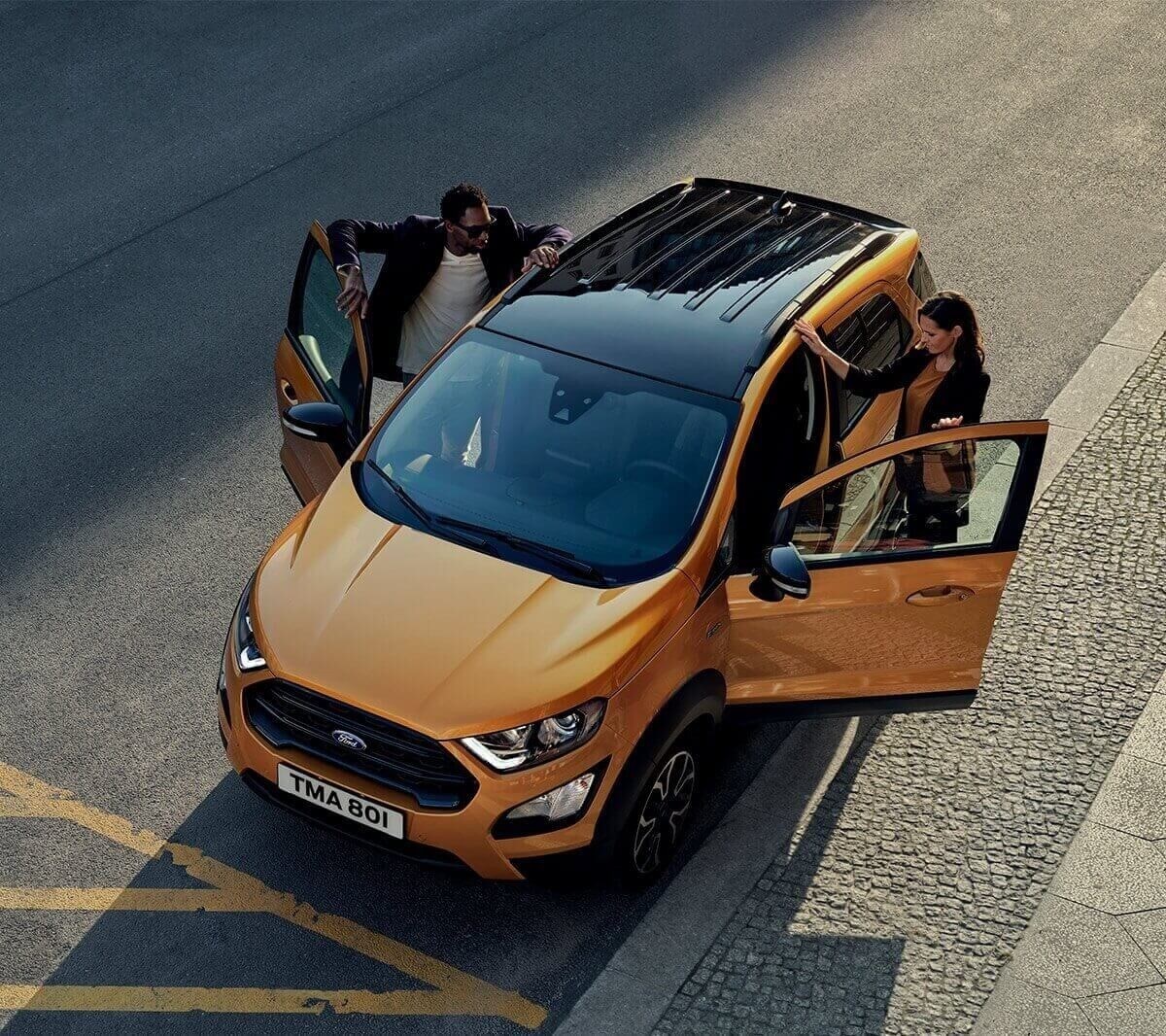 Ford EcoSport Active in Orange. Dreiviertelansicht von oben, Frau und Mann steigen in das Fahrzeug ein