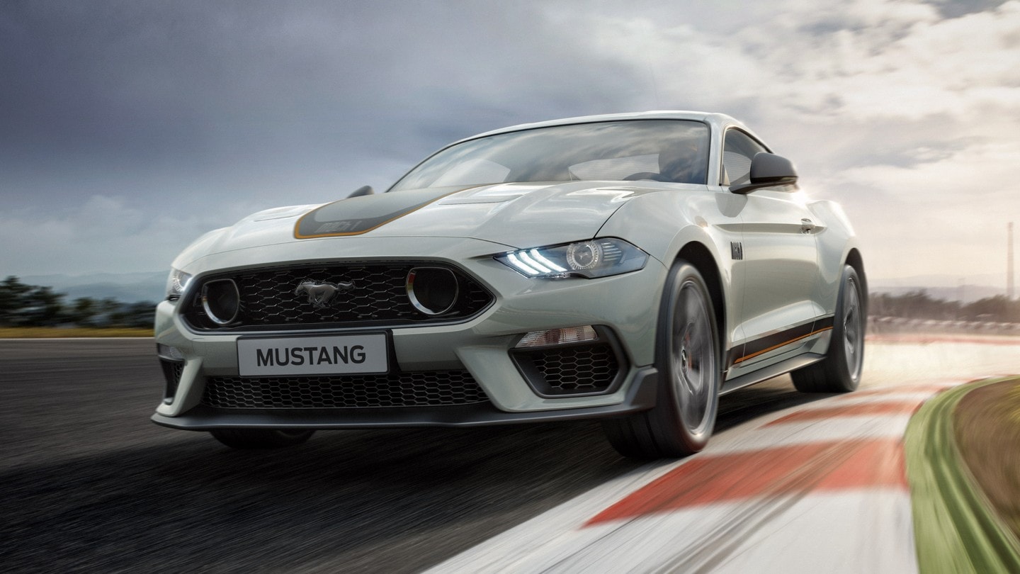 Ford Mustang Mach 1 in Weiß. Dreiviertelansicht von vorne, fahrend auf einer Strecke im Sonnenuntergang