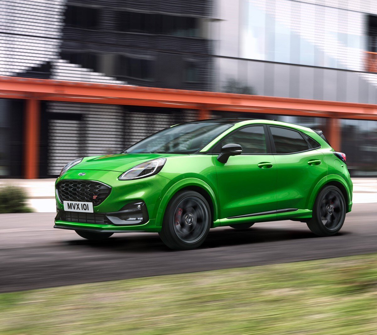Ford Puma ST in Grün. Dreiviertel-Frontansicht, fahrend auf einer Straße vor mordernem Gebäude