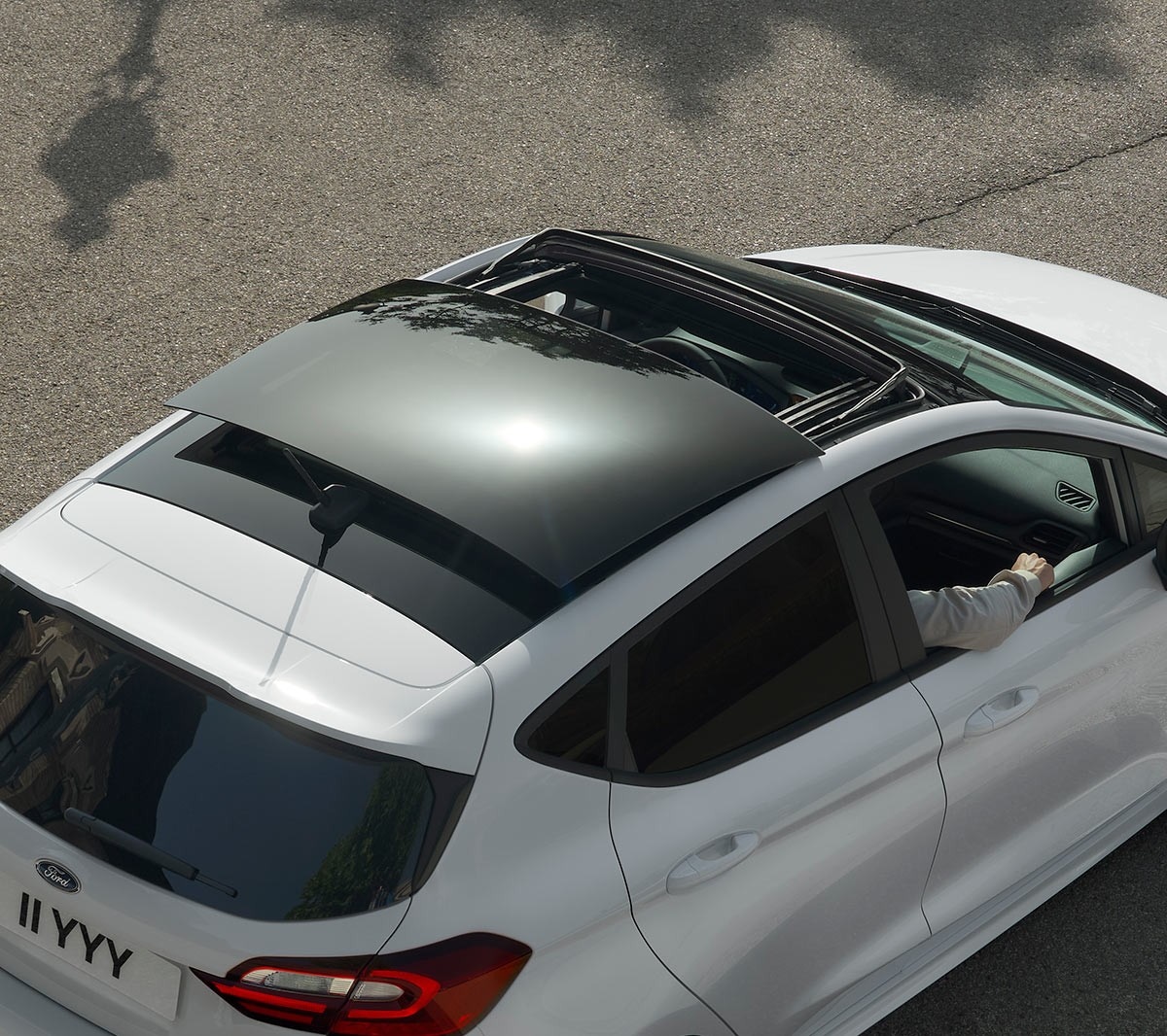 Ford Fiesta in Weiß. Blick von oben auf das Panorama-Schiebedach, auf einer Straße fahrend.