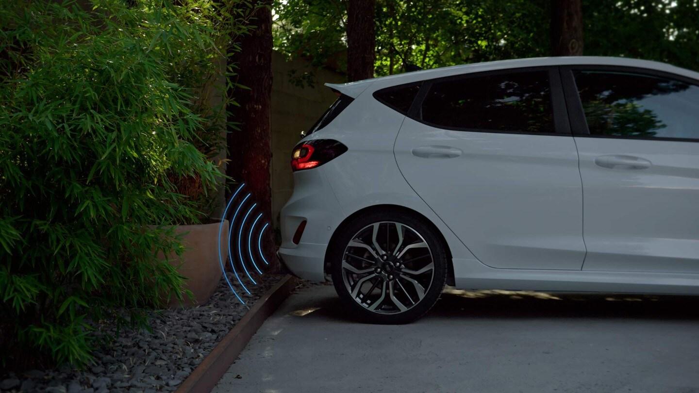 Ford Fiesta in Weiß. Seitenansicht, Parksituation mit Visualisierung Parkdistanzsensoren