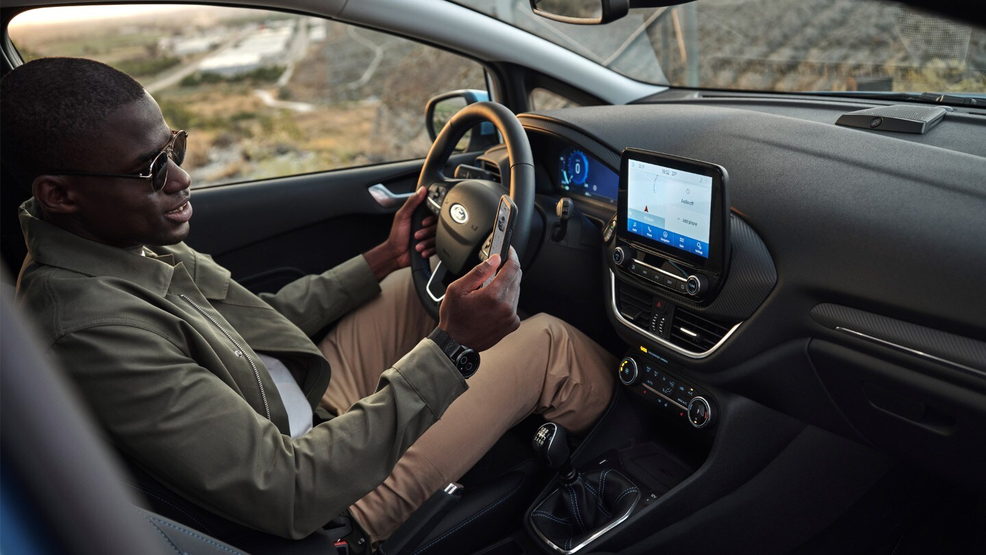 Ford Fiesta Innenraumansicht. Ein Mann auf dem Fahrersitz schaut auf sein Smartphone.