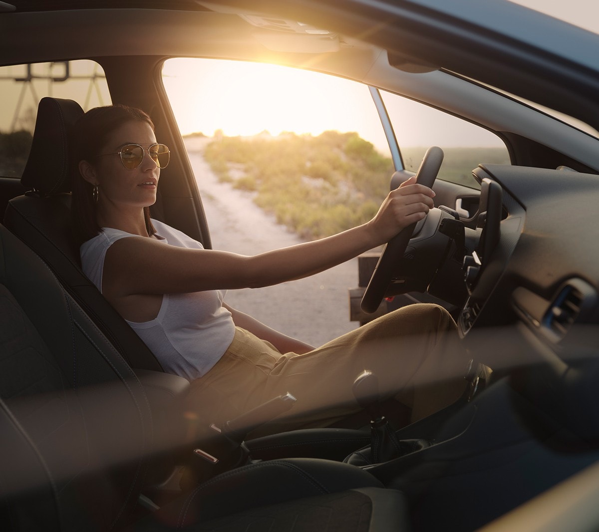 Ford Fiesta Innenraumansicht. Eine Frau sitz bei geöffneter Fahrertür auf dem Fahrersitz. Im Hintergrund ein Sonnenuntergang.