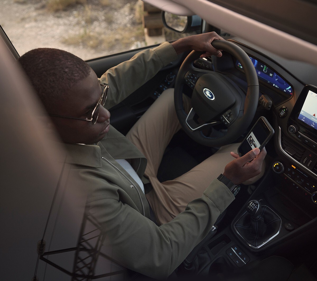 Ford Fiesta Innenraumansicht. Ein Mann auf dem Fahrersitz schaut auf sein Smartphone.