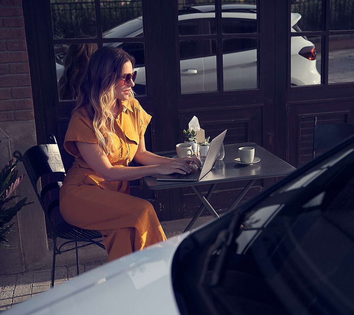 Ford Fiesta in Weiß. Detailansicht der Front, vor einem Café parkend mit Frau im Hintergrund.