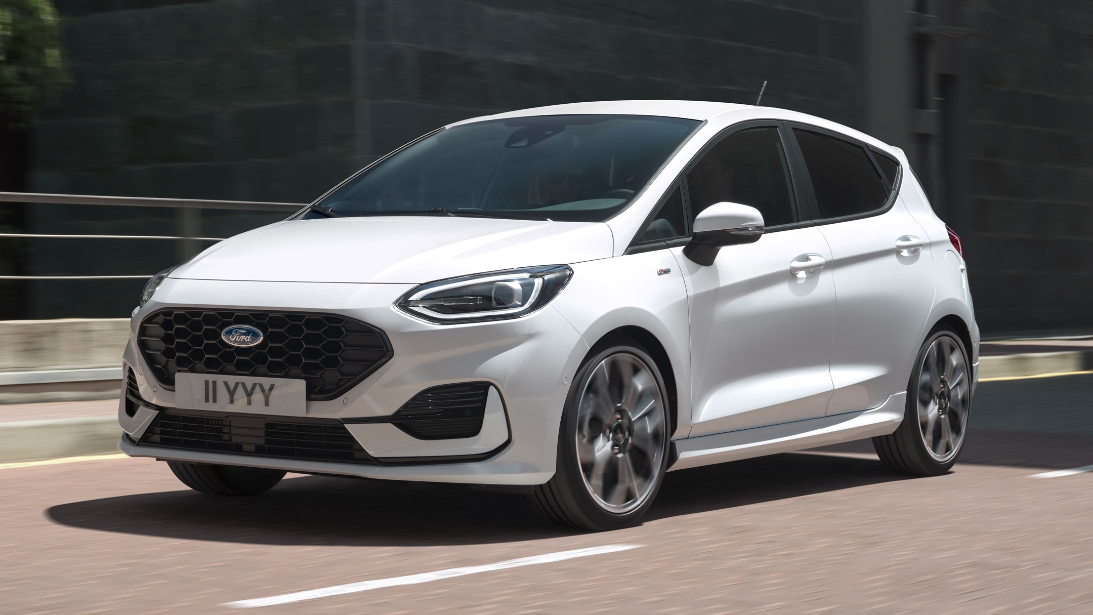 Ford Fiesta ST-Line in Weiß. Dreiviertelansicht, in einer Stadt fahrend mit modernen Gebäuden im Hintergrund.