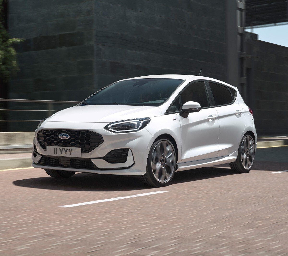 Ford Fiesta in Weiß. Dreiviertelansicht, in einer Stadt fahrend mit modernen Gebäuden im Hintergrund.