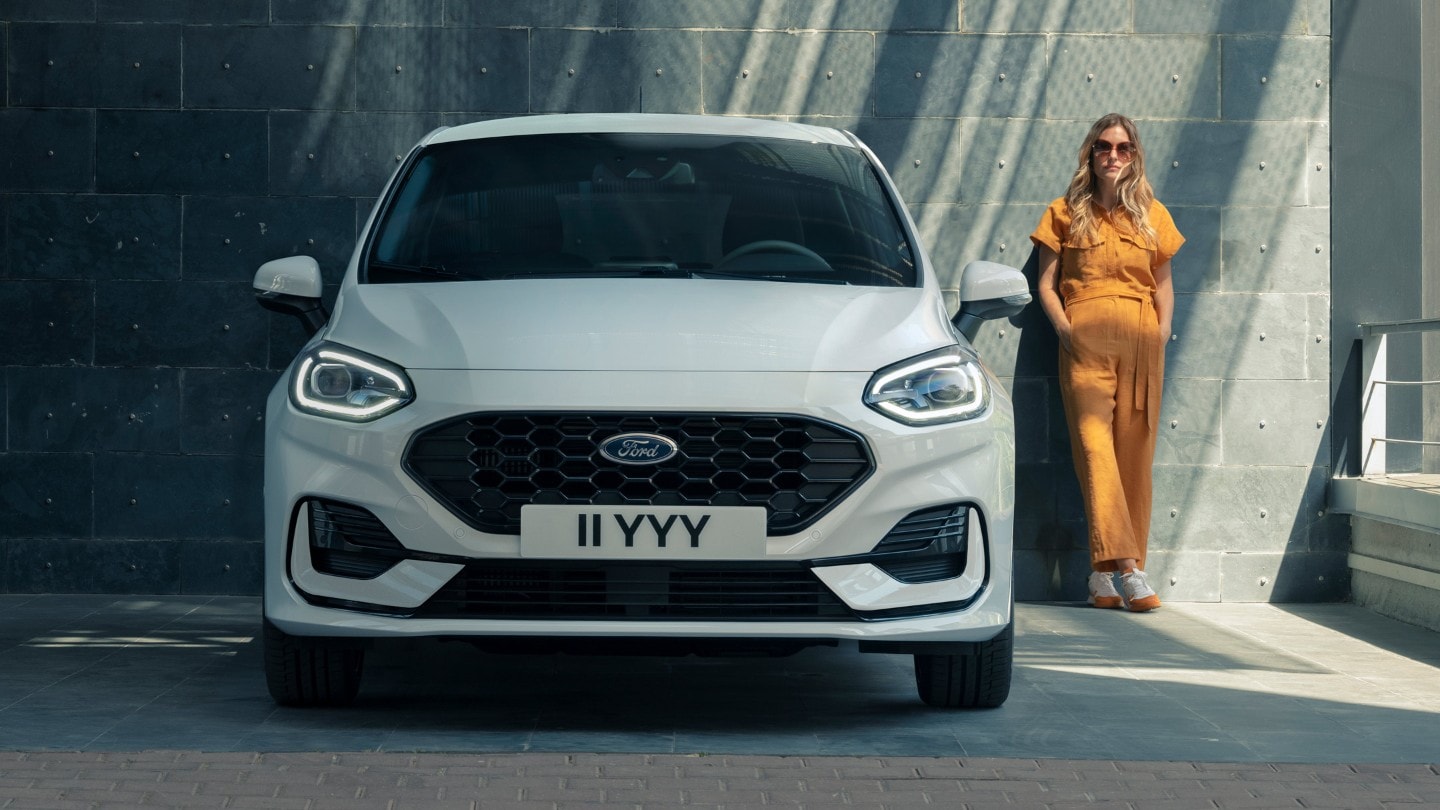 Ford Fiesta ST-Line in Weiß. Frontansicht, vor einem modernen Gebäude parkend mit Frau im Hintergrund.