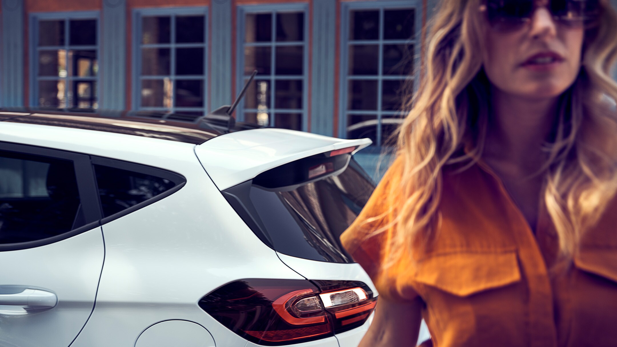 Ford Fiesta in Weiß. Seitenansicht des Hecks, vor einem Haus parkend mit Frau im Vordergrund.