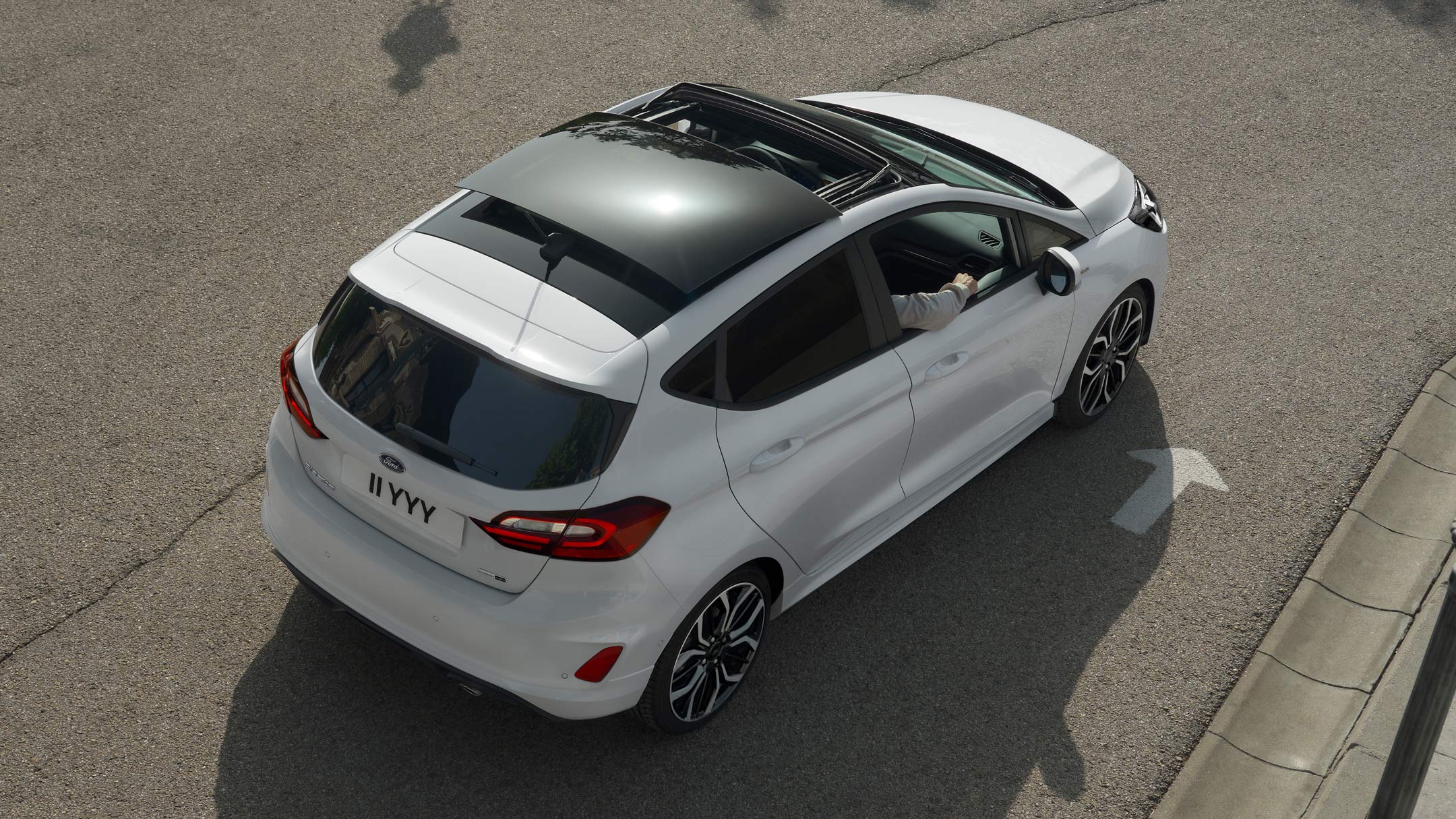 Ford Fiesta in Weiß. Blick von oben auf das Panorama-Schiebedach, auf einer Straße fahrend.