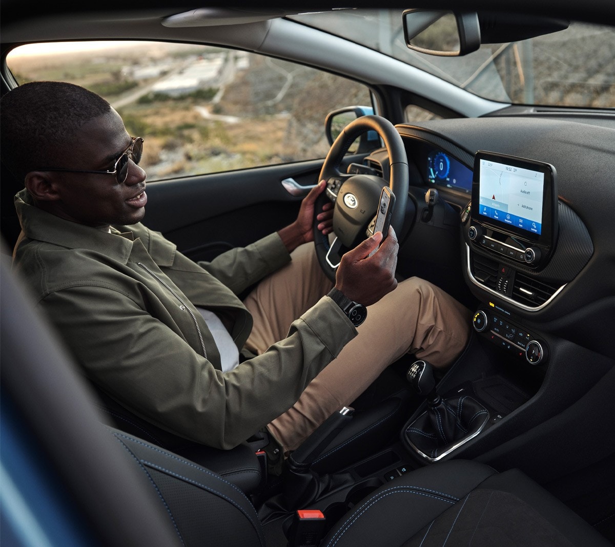 Ford Fiesta Innenraumansicht. Ein Mann auf dem Fahrersitz schaut auf sein Smartphone.