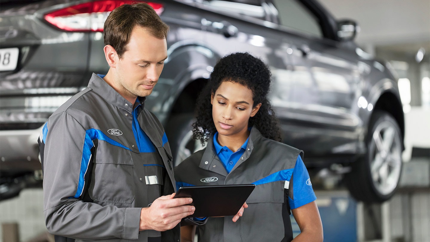 Zwei Ford-Servicetechniker in der Werkstatt schauen auf ein Tablet.