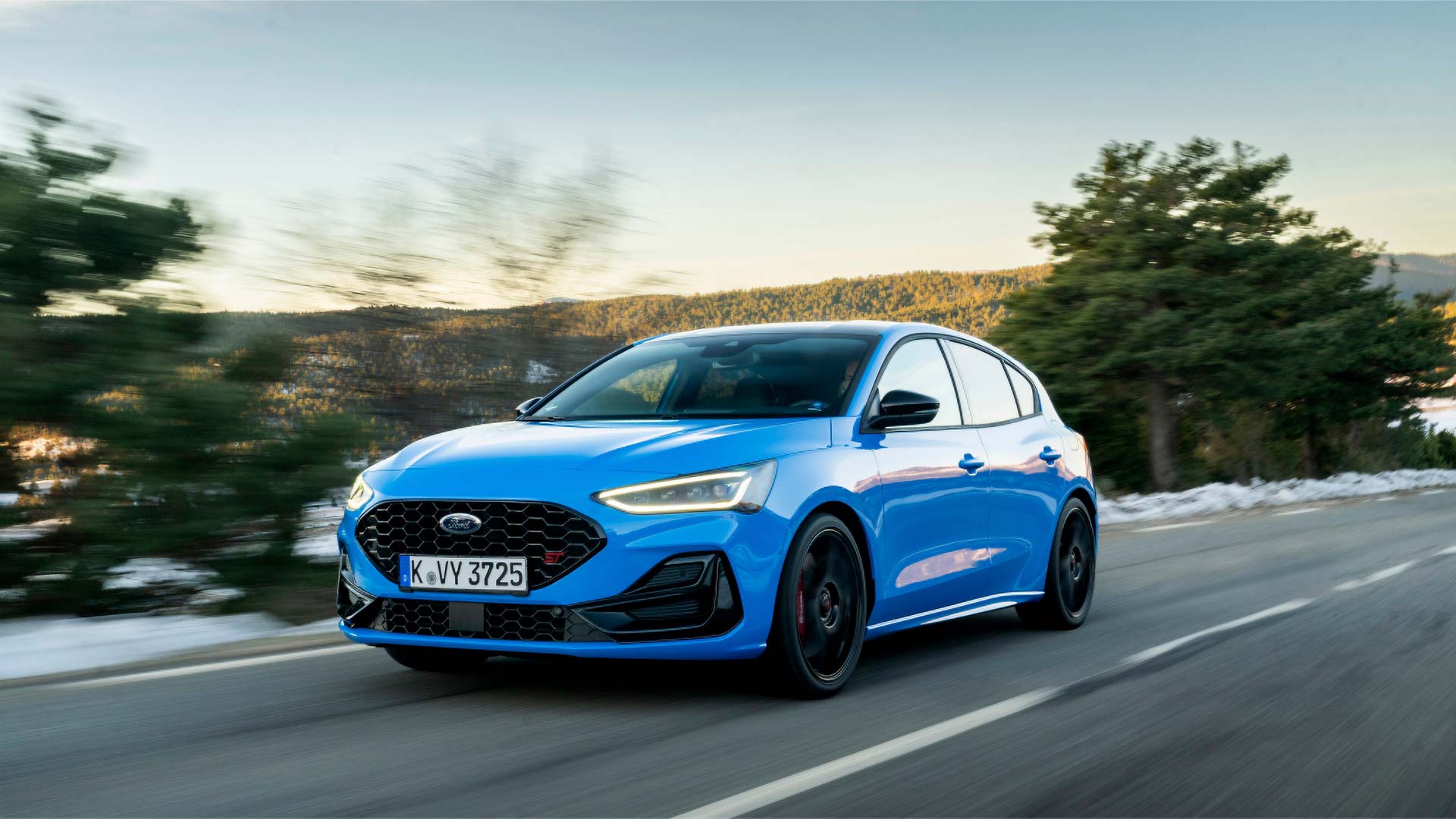 Ford Focus ST in Blau. Dreiviertelansicht, fahrend auf einer Straße. Bäume im Hintergrund.