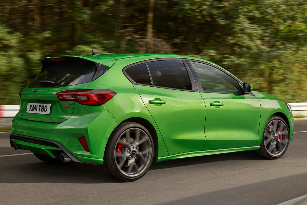 Ford Focus ST in Grün. Hecktansicht, fahrend auf einer Straße. Bäume im Hintergrund.