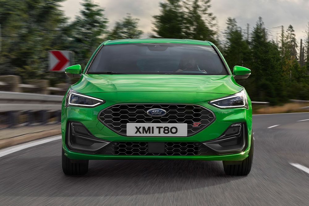 Ford Focus ST in Grün. Frontansicht, auf einer Straße fahrend. Bäume im Hintergrund.