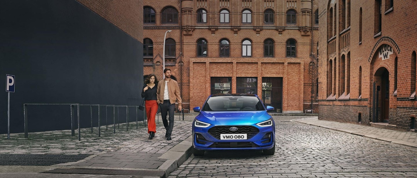 Ford Focus in Blau. Frontansicht, parkt vor einem Ziegelsteingebäude