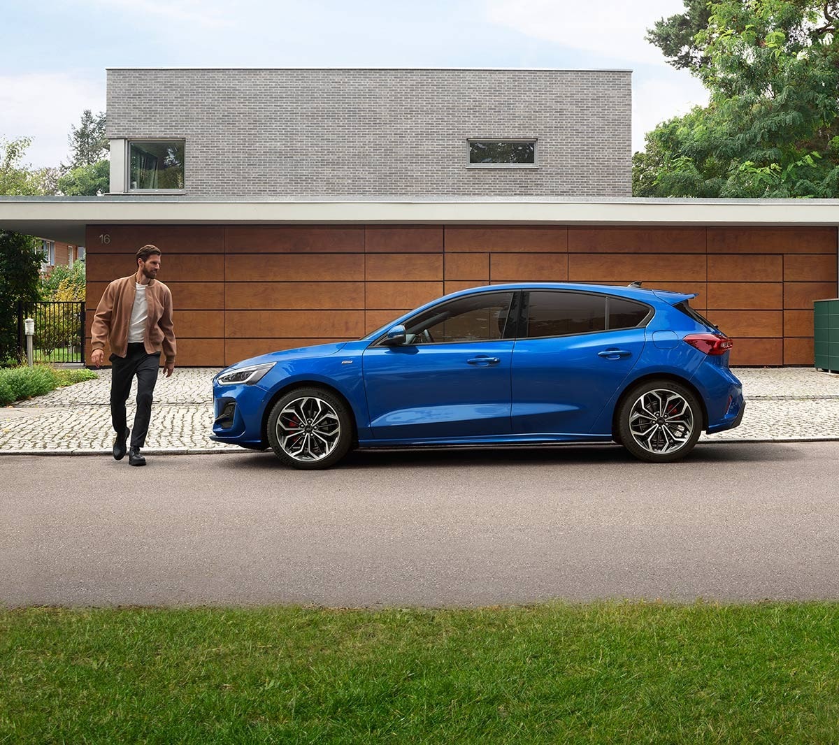 Ford Focus ST-Line in Blau. Seitenansicht, vor einem modernen Haus parkend. Ein Mann läuft daneben.