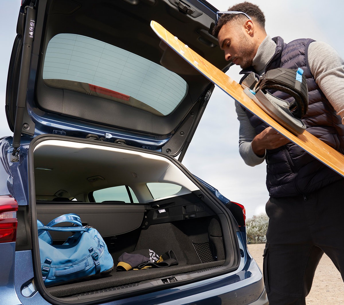 Ford Focus Active in Blau. Heckansicht, ein Mann verstaut ein Snowboard im Kofferraum.