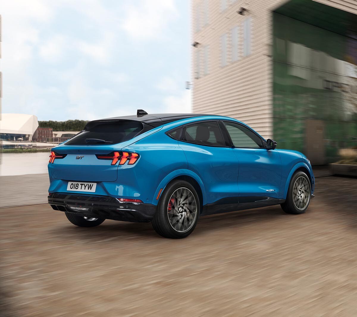 Ford Mustang Mach-E GT in Blau. Dreiviertelansicht von hinten, fahrend in einem Industriegebiet