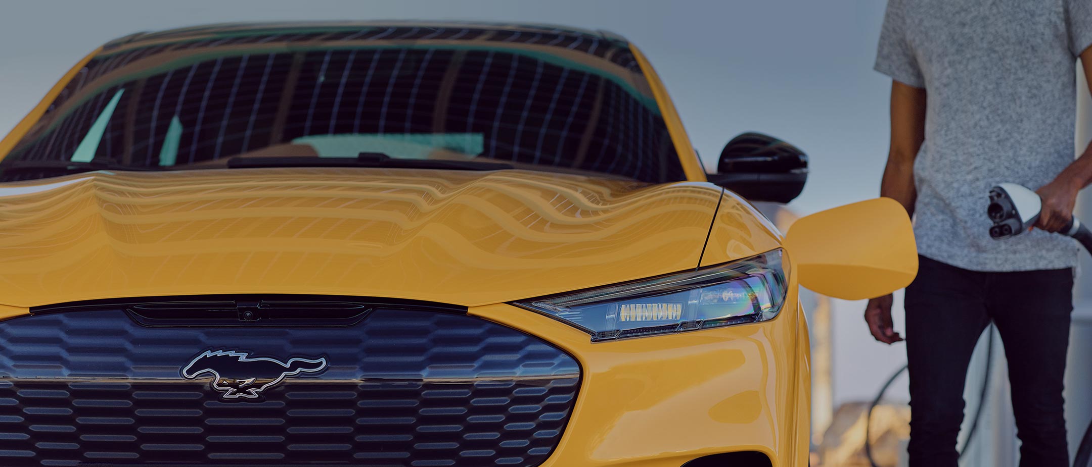 Ford Mustang Mach-E GT in Gelb. Frontansicht, Mann schließt Ladekabel an