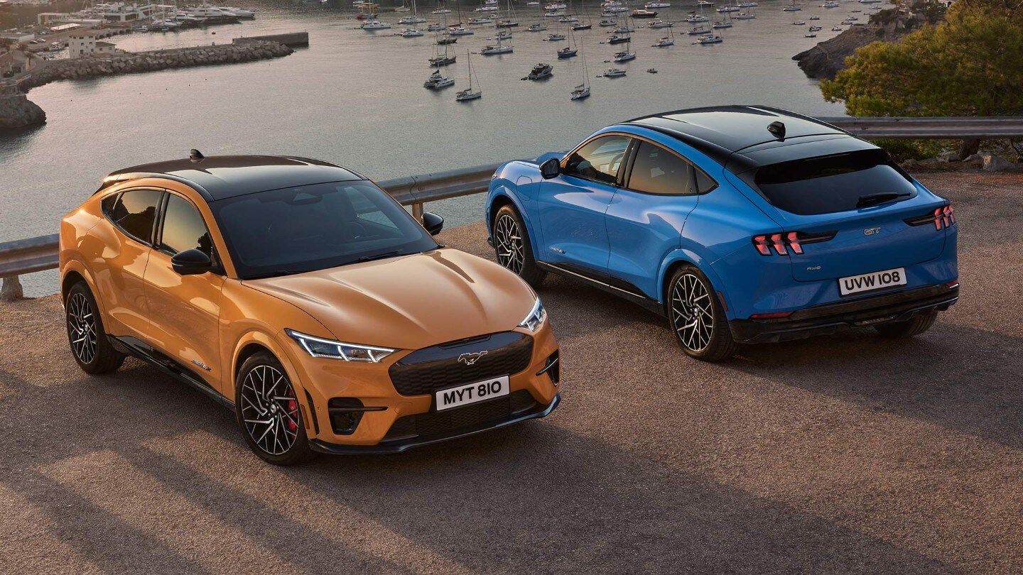 Ford Mustang Mach-E GT in Orange und Blau. Ansicht von oben, vor einem See parkend.