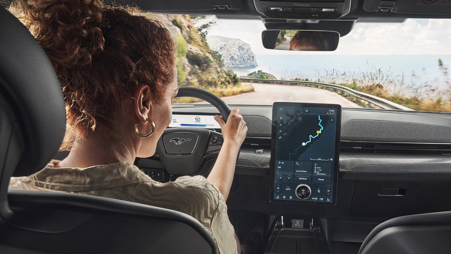 Ford Mustang Mach-E Innenraum. Frau sitzt im Auto und sieht auf den Touchscreen.