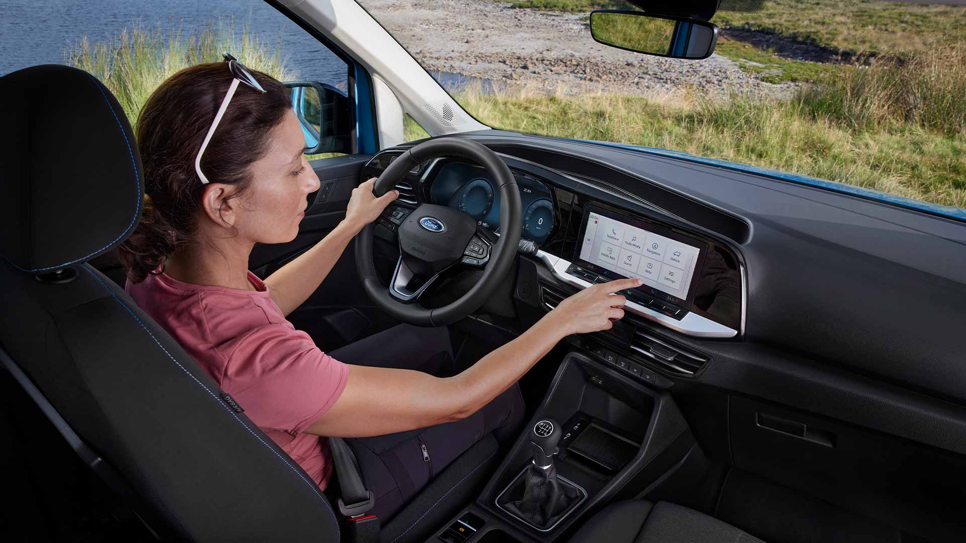 Ford Tourneo Connect Innenraum. Ansicht Fahrerkabine mit einer Person am Fahrersitz, die den Touchscreen bedient.