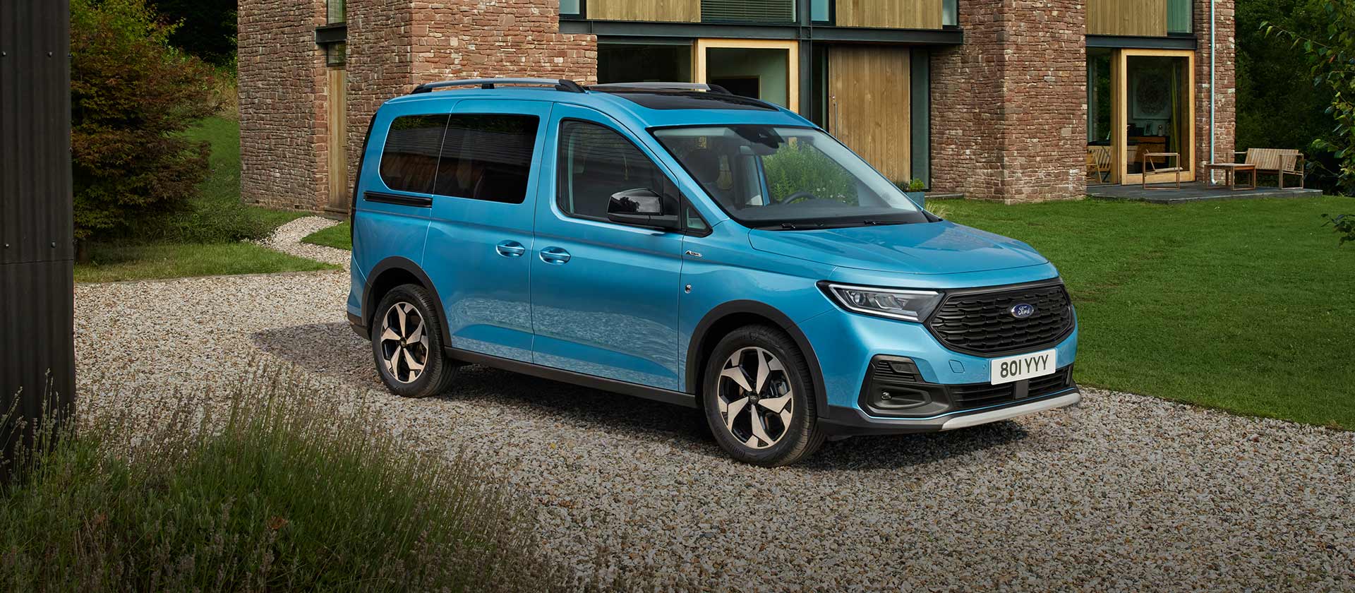 Ford Tourneo Connect Active in Blau. Dreiviertelansicht, parkt auf Kiesweg vor Wohnhaus. 