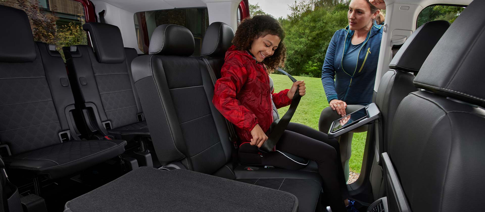 Ford Tourneo Connect Innenraum. Ansicht der 2. und 3. Sitzreihe, eine Person schnallt sich an.