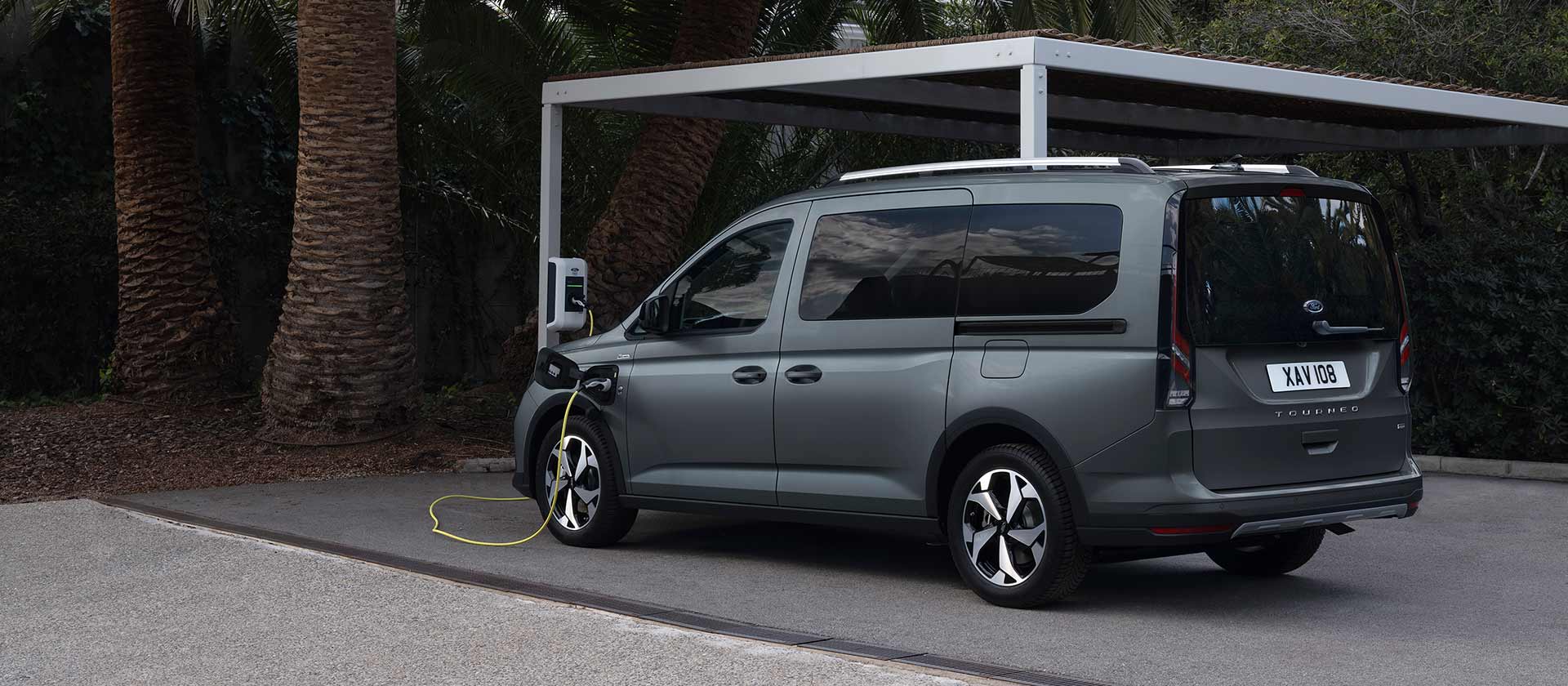 Ford Tourneo Connect in Grau. Dreiviertelansicht, angeschlossen an einer Ladestation. 