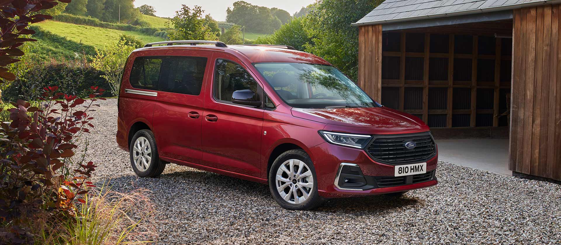 Ford Tourneo Connect Titanium in Rot. Dreiviertelansicht, parkt auf Kiesweg vor einem Haus.