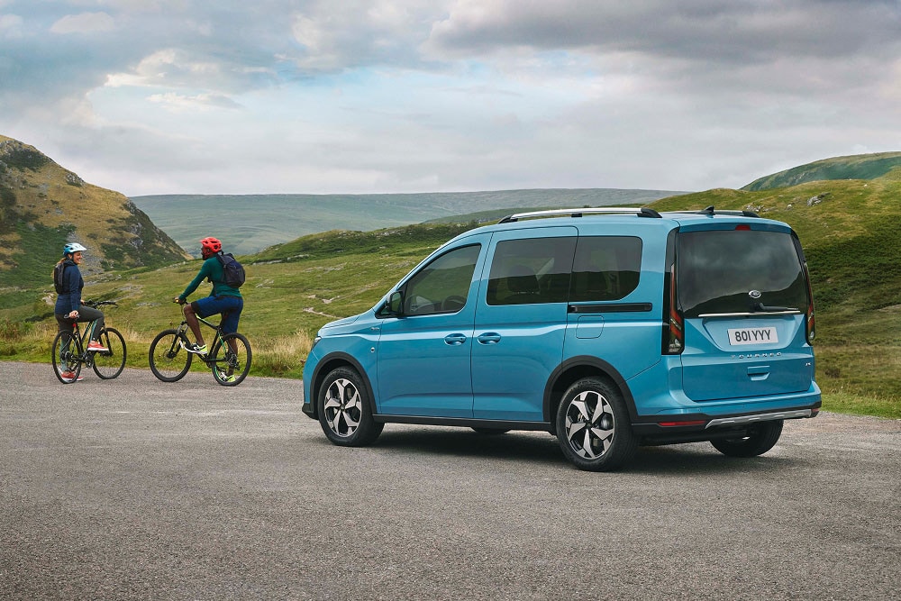 Ford Tourneo Connect in Blau. Dreiviertelansicht, geparkt auf einer Landstraße neben zwei Fahrradfahrern.