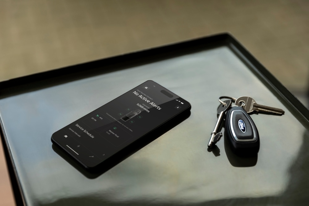 Smartphone mit geöffneter Ford App. Daneben liegt ein Ford Fahrzeugschlüssel.