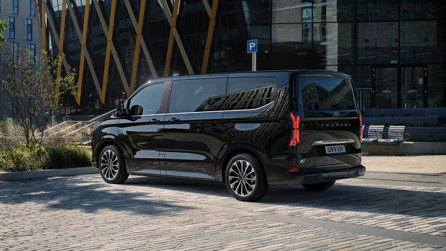 Ford Tourneo Custom in Schwarz. Heckansicht, geparkt auf einem Parkplatz vor modernen Gebäuden