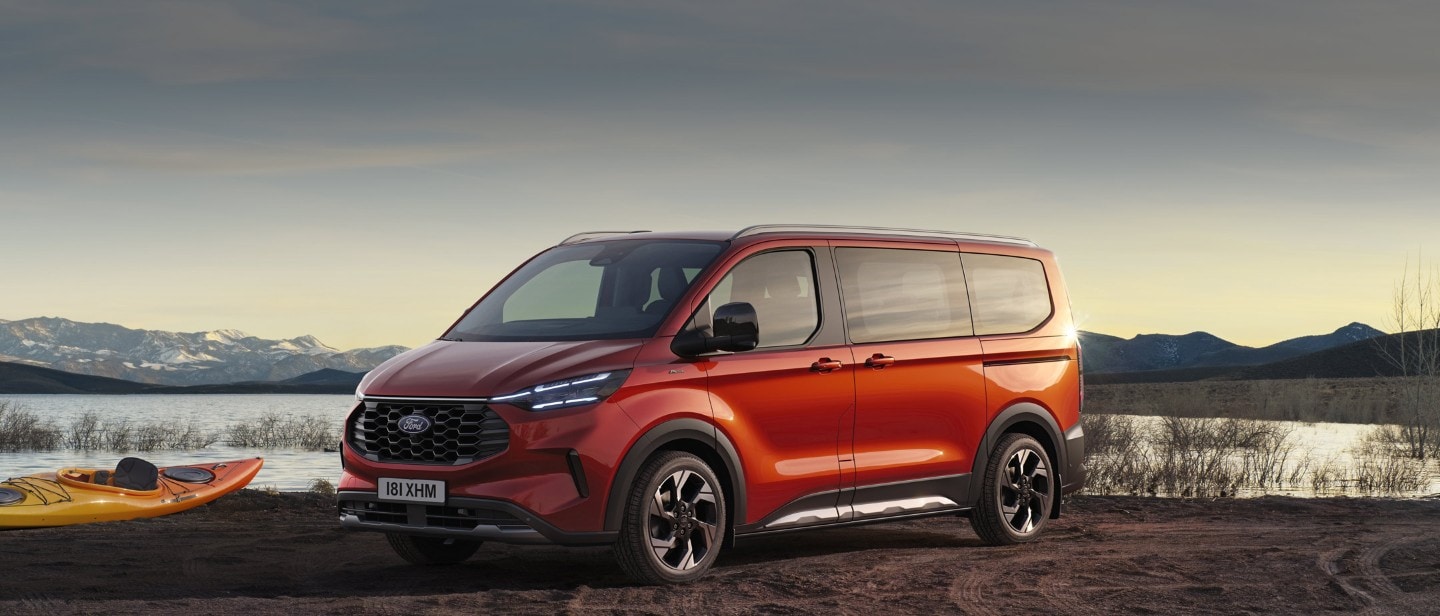 Ford Tourneo Custom in Orange. Dreiviertelansicht, vor einem Flussufer geparkt