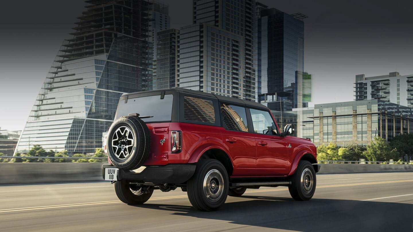 Ford Bronco in Rot. Heckansicht, fahrend durch eine Stadt.