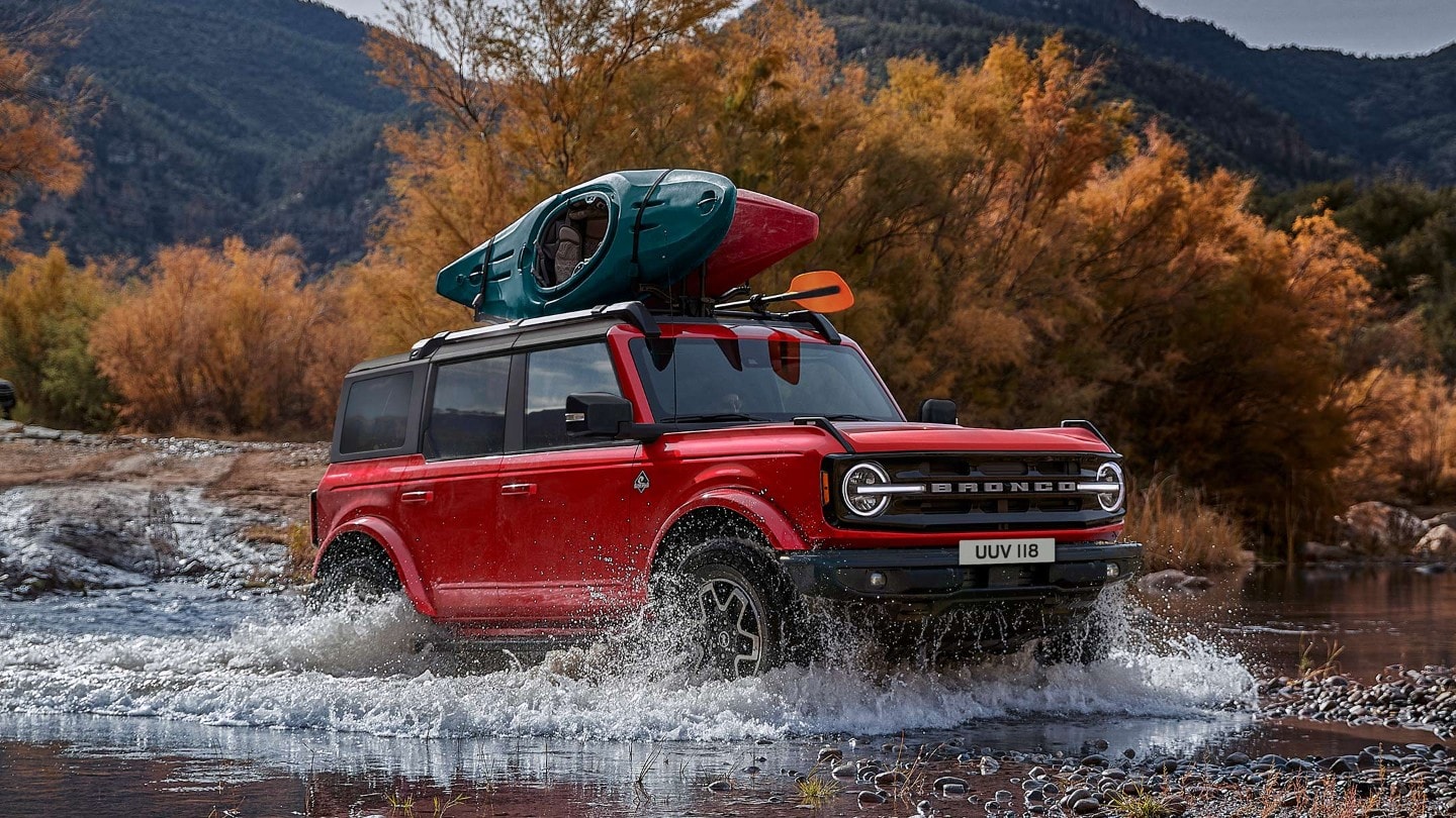 Ford Bronco in Rot. Dreiviertelansicht, fahrend in felsiger Landschaft durch einen Wasserlauf