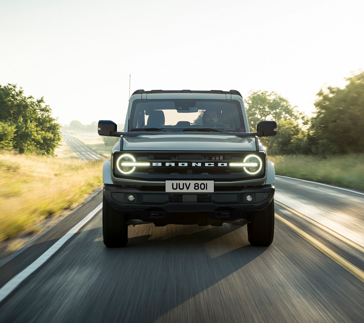Ford Bronco in Grau. Frontansicht, fahrend auf einer Landstraße.