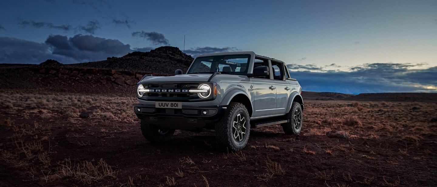 Ford Bronco in Grau. Frontansicht, stehend bei Dämmerung am Feldrand