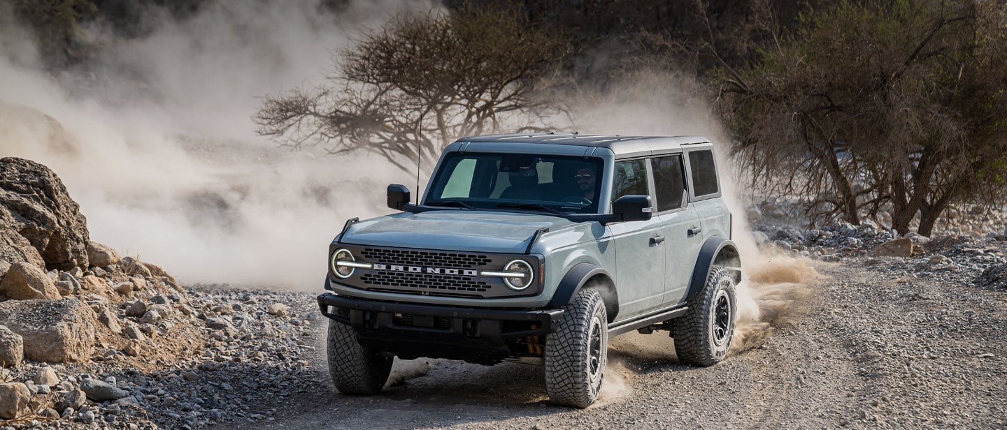 Ford Bronco in Grau. Dreiviertelansicht, fahrend auf staubigem Schotterweg um eine Kurve