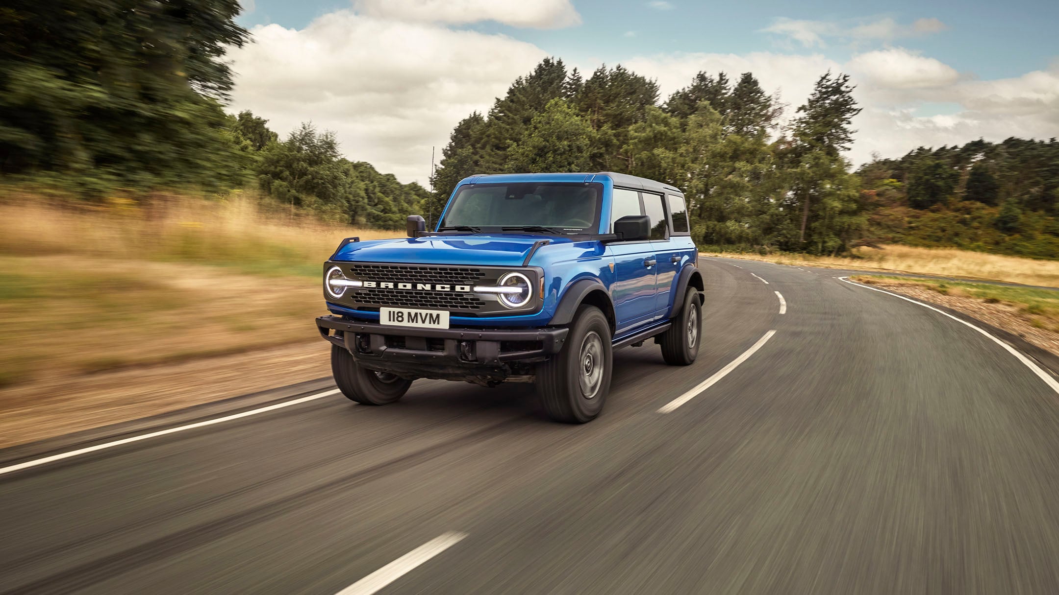 Ford Bronco in Blau. Dreiviertelansicht, fahrend auf einer Landstraße