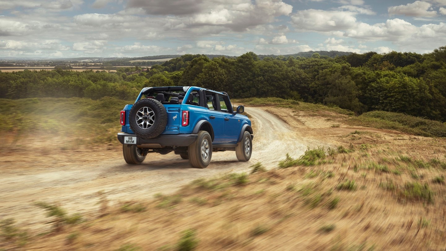 Ford Bronco in Blau. Heckansicht, fahrend auf einem Feldweg