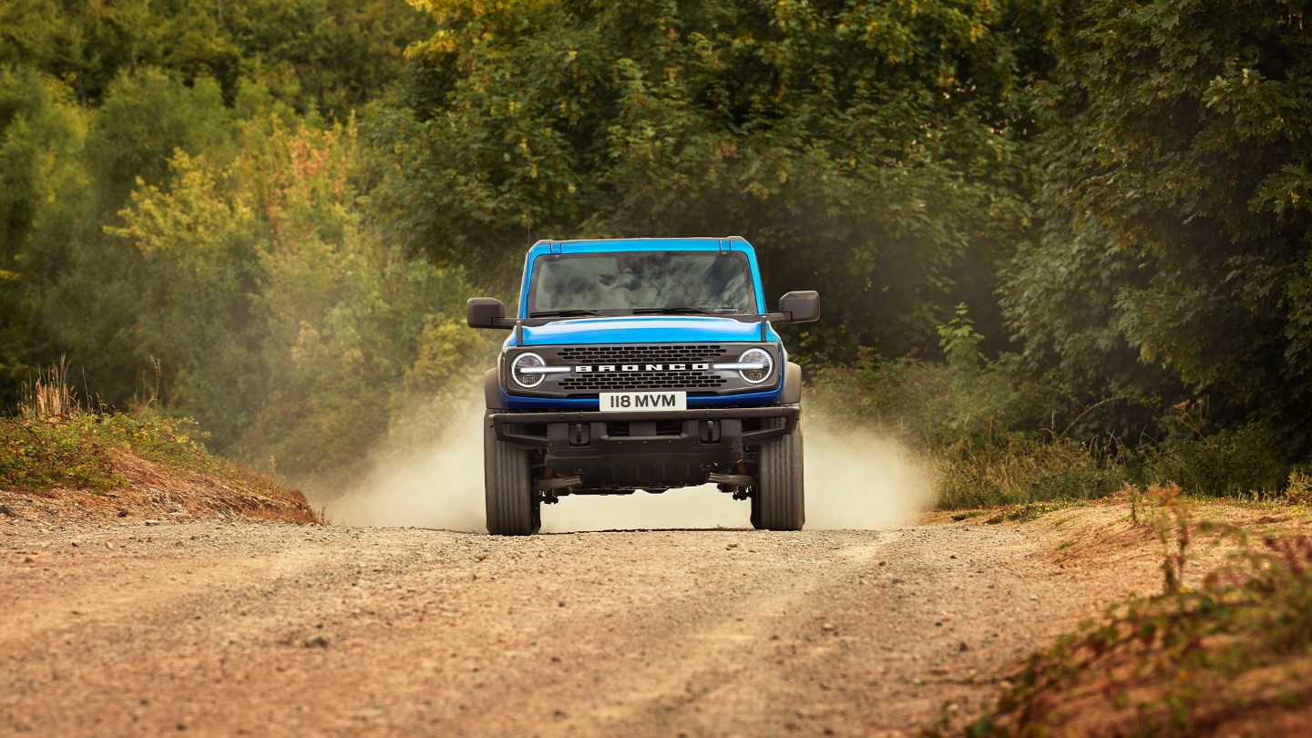 Ford Bronco in Blau. Frontansicht, fährt auf einem staubigen Weg