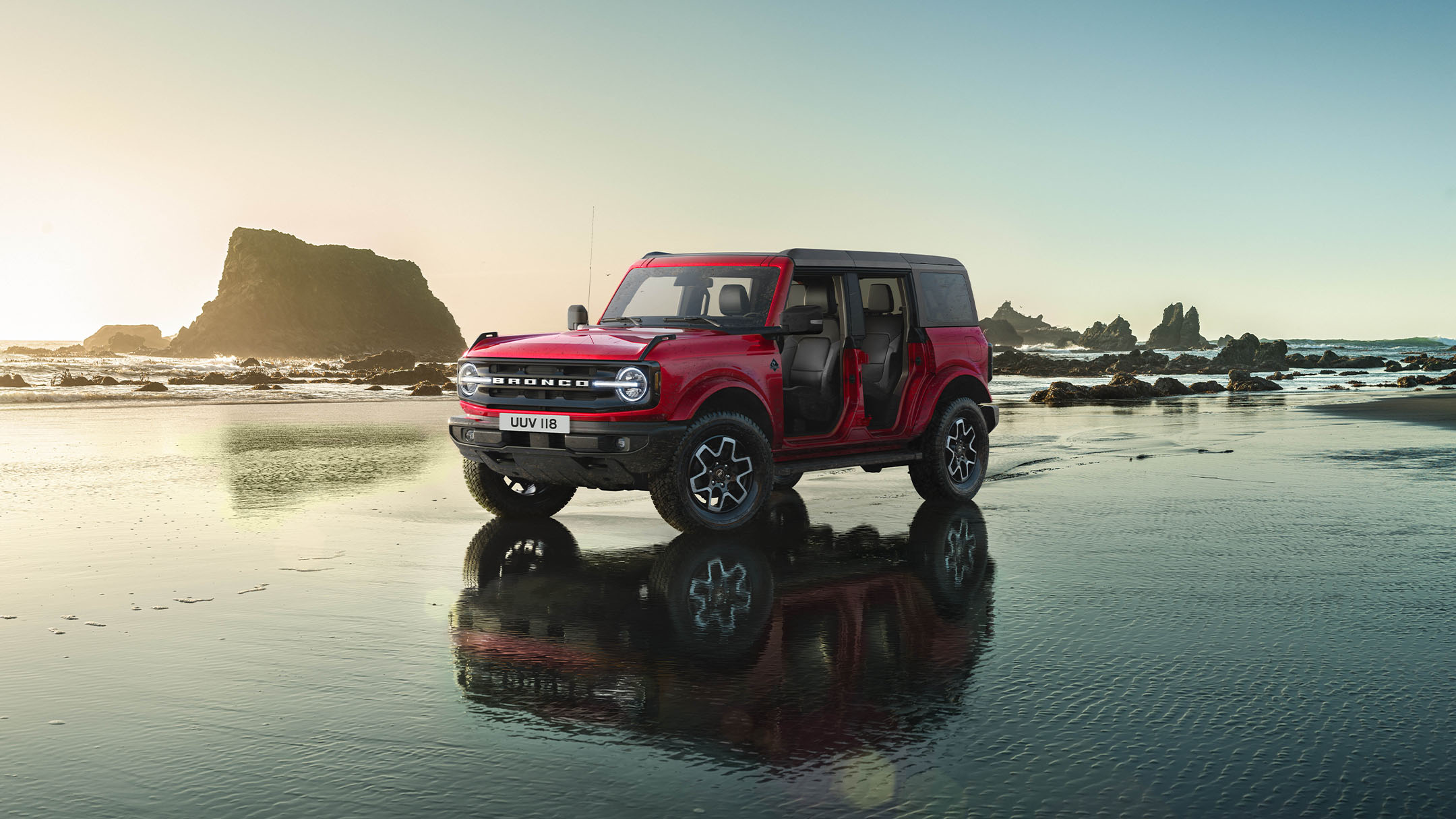 Ford Bronco in Rot. Dreiviertelansicht, stehend mit abgenommenen Türen auf einer mit Wasser bedeckten Fläche