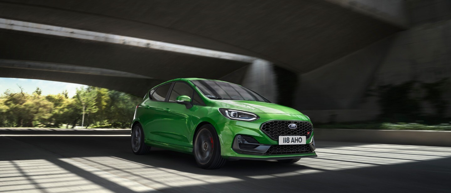 Ford Fiesta ST in Grün. Dreiviertelansicht, fährt unter einer Brücke