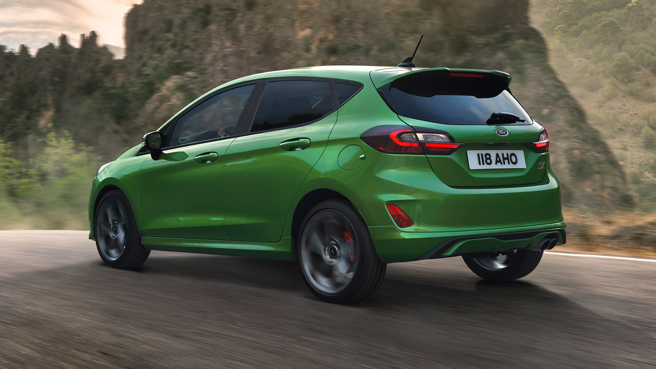 Ford Fiesta ST in Grün. Dreiviertelansicht, auf Straße in den Bergen fahrend.