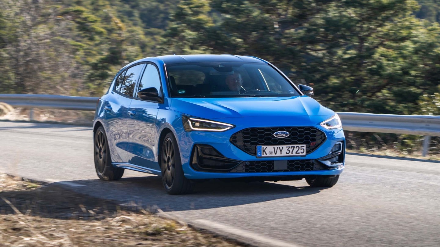 Ford Focus ST in Blau. Dreiviertelansicht, fahrend auf einer Straße. Bäume im Hintergrund.