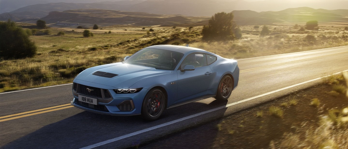 Ford Mustang in Blau. Dreiviertelansicht, fahrend auf einer Landstraße bei Sonnenuntergang.