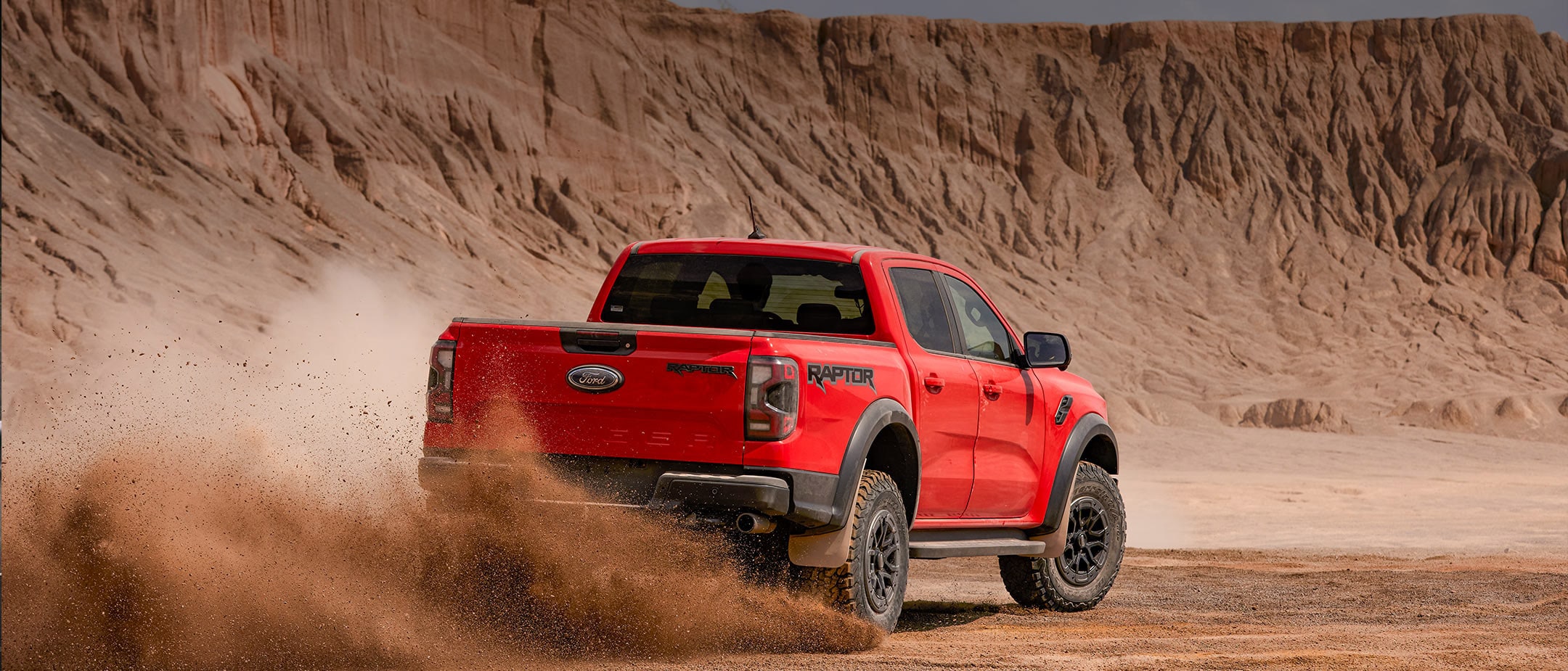 Ford Ranger Raptor in Rot. Heckansicht, fährt in einer Wüstenlandschaft